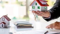 mano de un hombre mostrando una vivienda con sus llaves y papeles de un préstamo hipotecario