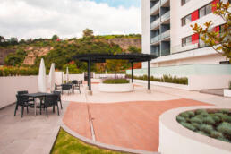 Vista de las áreas verdes del desarrollo inmobiliario de Real de Monteza. Mesas, sillas y sombrillas colocadas en la terraza del edificio.