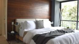 Interior de una habitación de un departamento de Real de Monteza. Cama con almohadas, sábanas, cobijas y una mesa de servicio para cama. Lámparas a los costados.